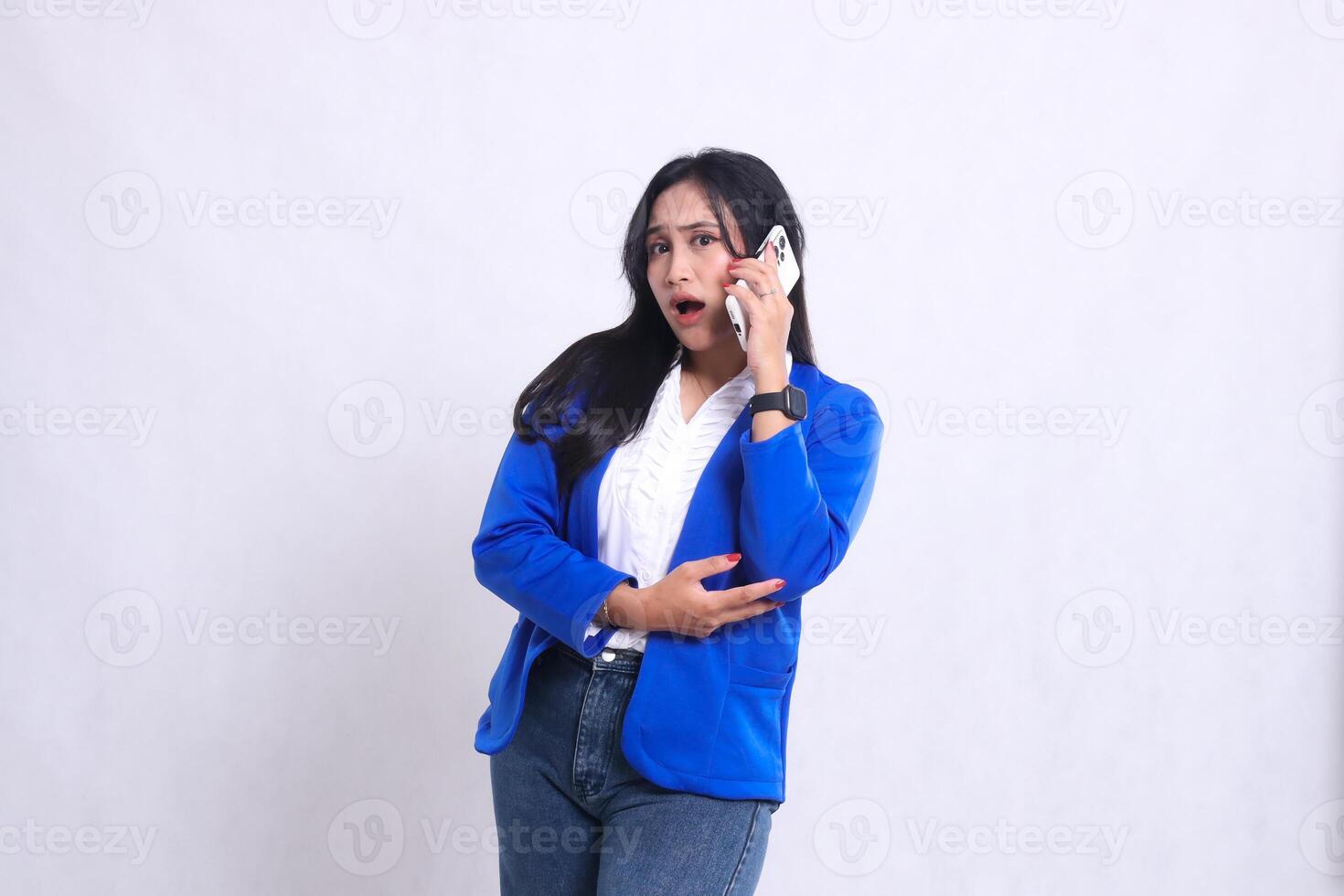 beautiful adult office woman wearing blue formal suit standing surprised to camera while talking on phone using smartphone mobile phone isolated white background. for technology, lifestyle photo