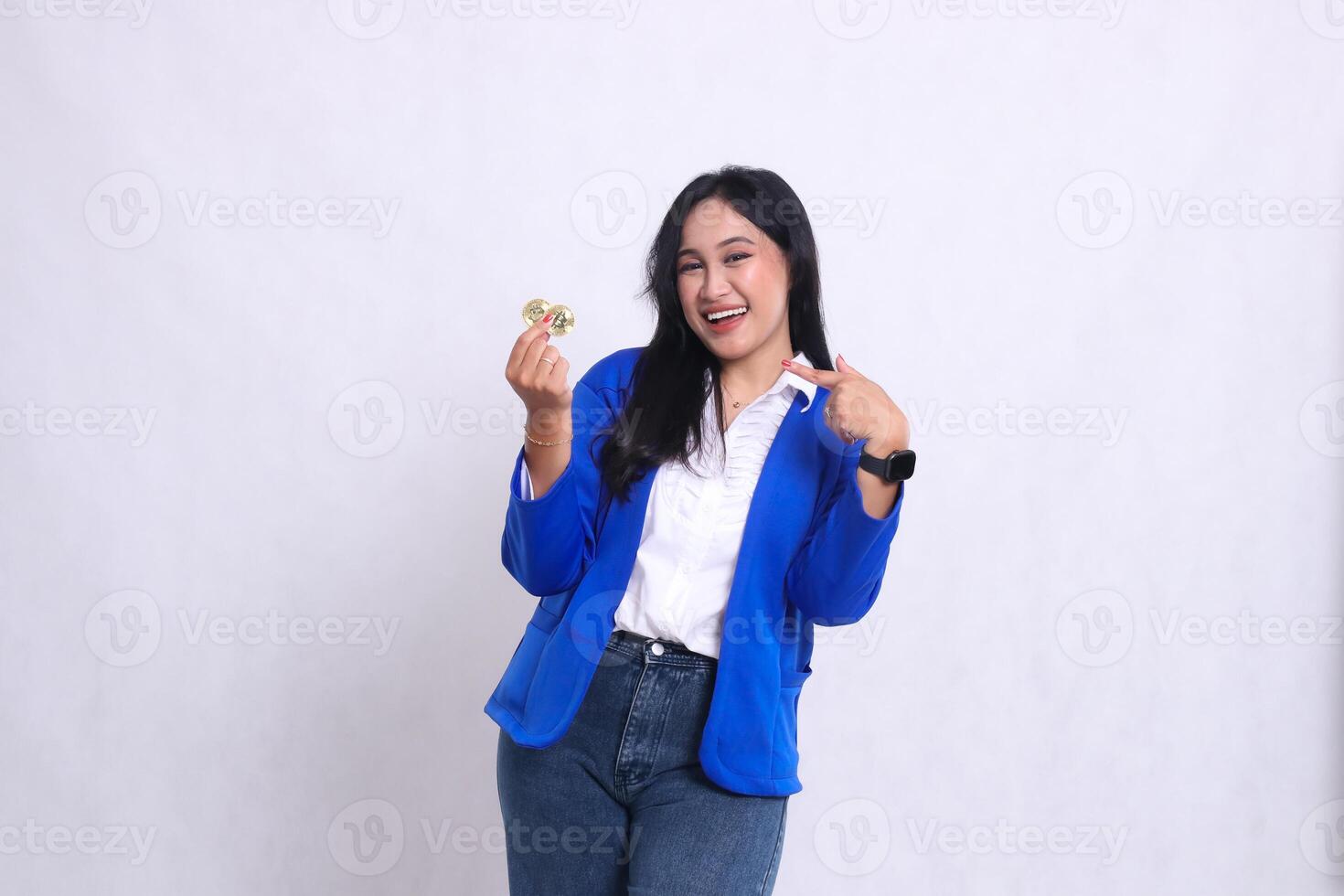 beautiful mature office woman wearing blue formal suit standing cheerfully to camera holding bitcoin while pointing at it isolated white background. for transaction, investment, business content photo
