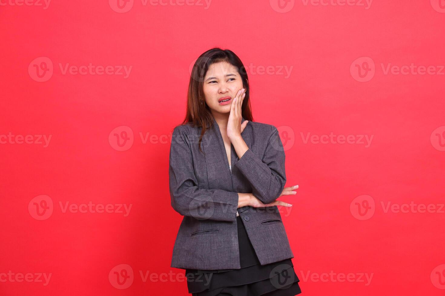 Asian office girl expression in pain, toothache candid, wearing a gray jacket and black mini skirt on a red background. for health, business and advertising concepts photo