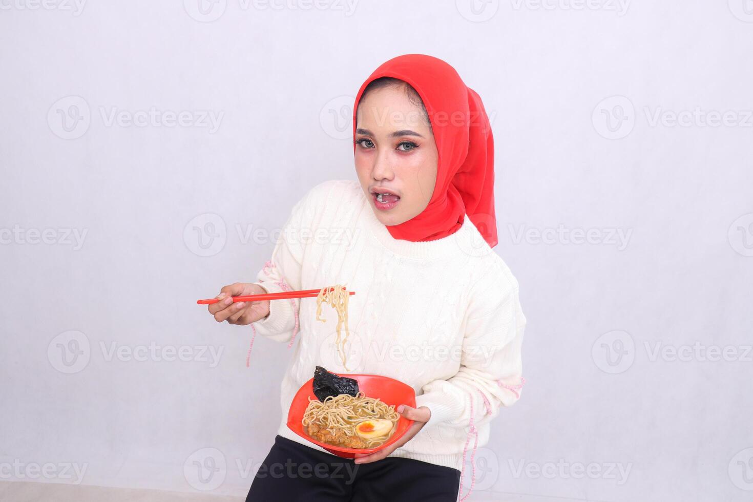 indonesia woman wearing a hijab is surprised to see the camera top angle carrying noodles with chopsticks and a bowl containing ramen Chinese food. Beautiful Muslim women are used for content photo