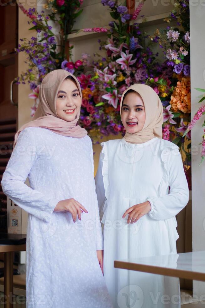 a pair of young muslim woman in hijab smile to the camera stand formally in the outdoor area of restaurant. for technology, transaction, business, lifestyle content photo