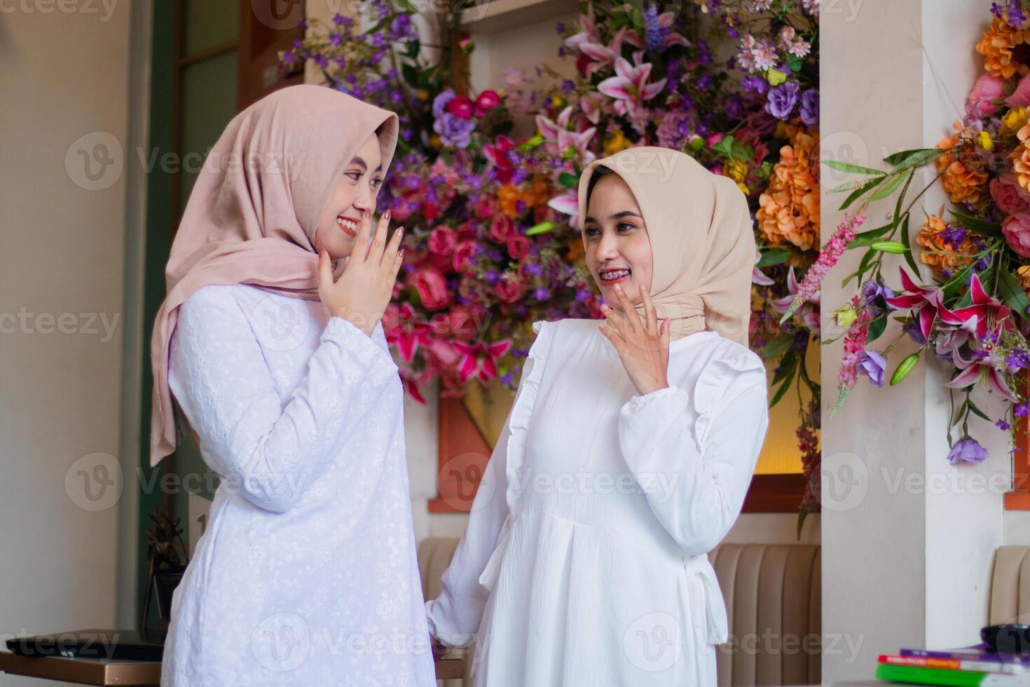 a pair of adult muslim girl in hijab look at each other laughing standing in the outdoor area of restaurant. for technology, transaction, business, lifestyle photo