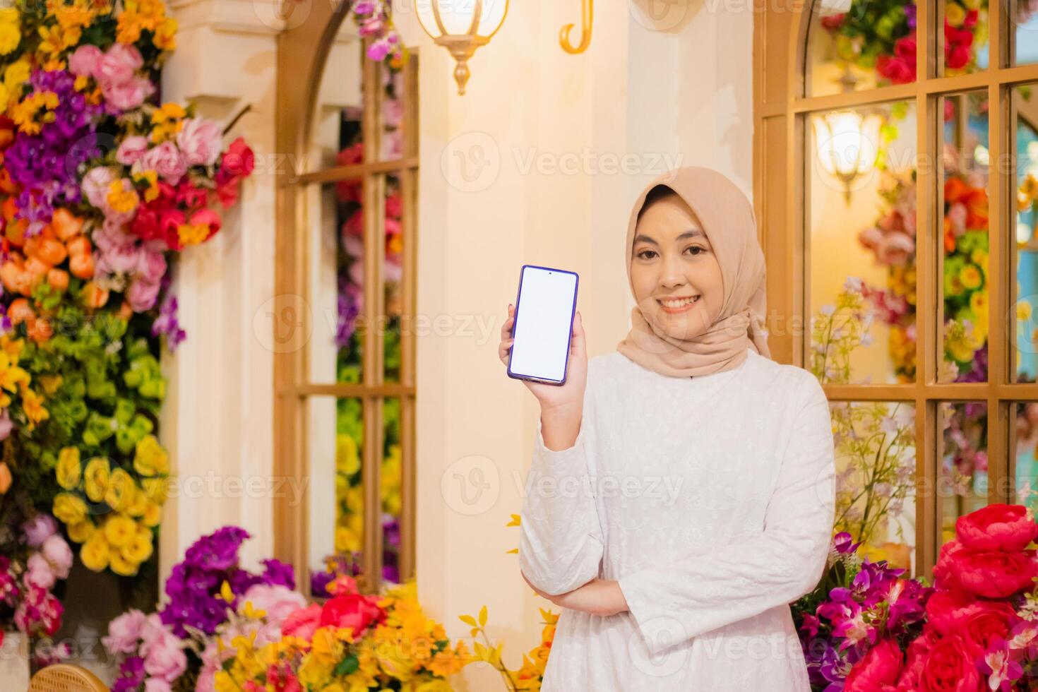 young woman hijab wearing white dress muslim cheerful to camera hand showing mobile phone screen, smartphone, cellphone inside luxury restaurant. for fashion, beauty, lifestyle content photo
