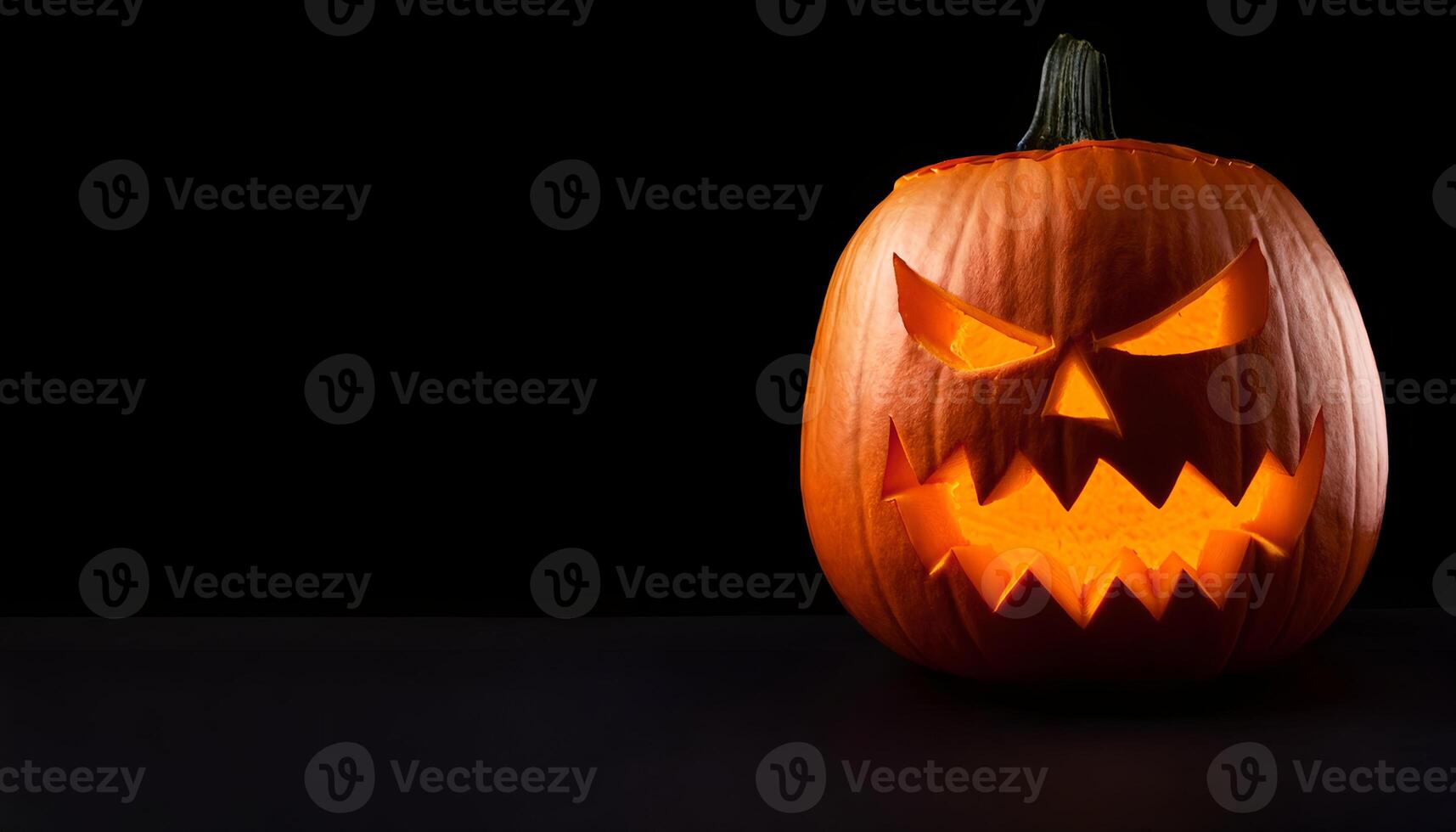 A pumpkin carved into a classic jack-o'-lantern with a menacing face, glowing brightly from within, set against a stark black background for dramatic effect. photo