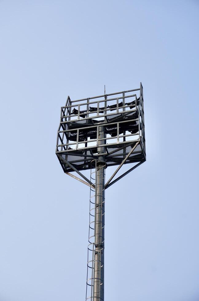 Tall floodlight stadium lamp post tall metal structure from behind view isolated on vertical blue sky background. photo