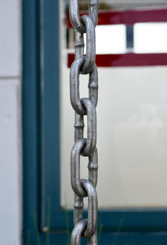 Metal iron silver chain object isolated on vertical ratio outdoor building wall and window frame exterior background. photo