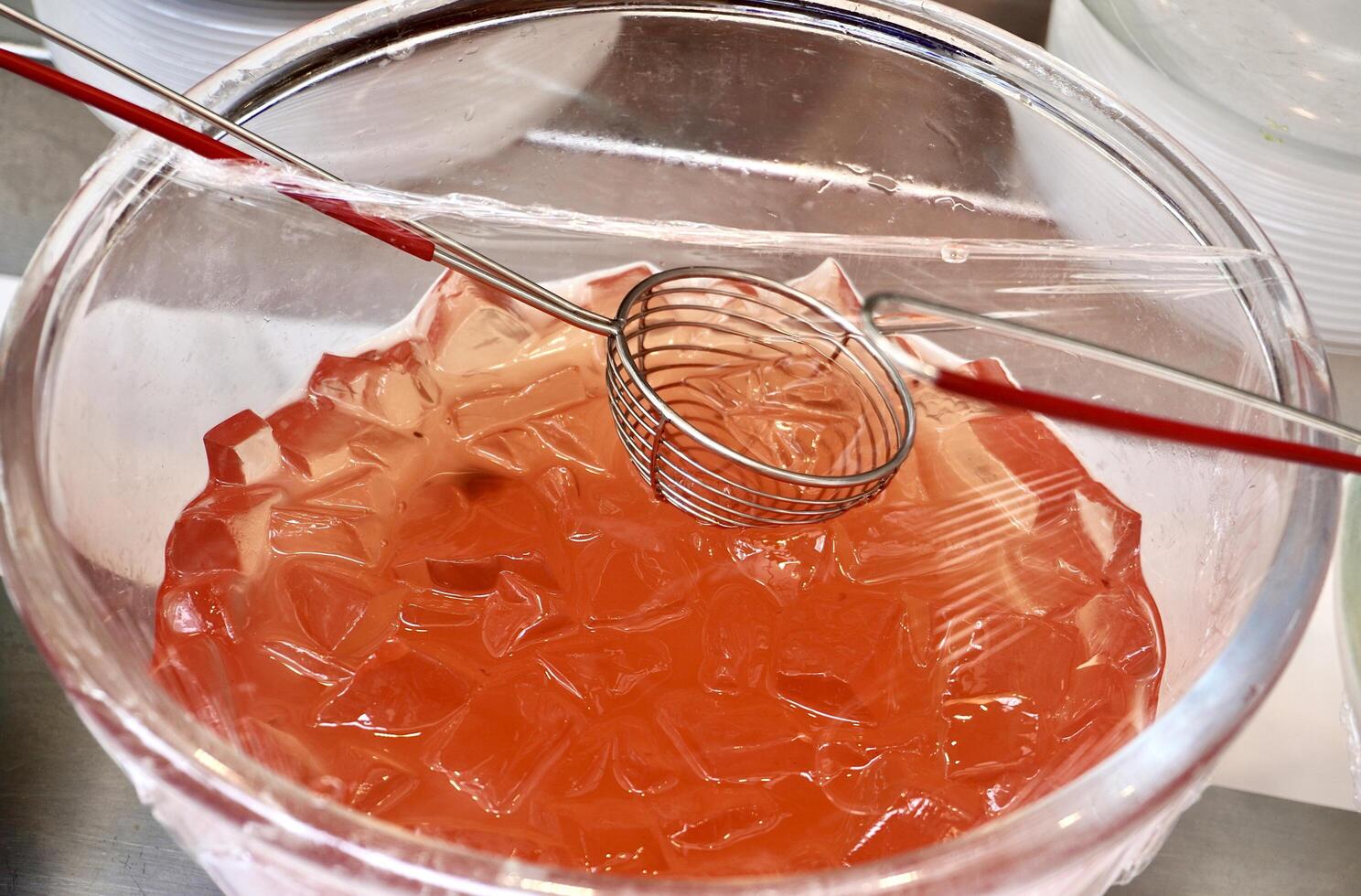 Sweet and delicious orange agar-agar jelly dessert toppings in glass bowl with plastic cover and spoon isolated on horizontal ratio background. photo