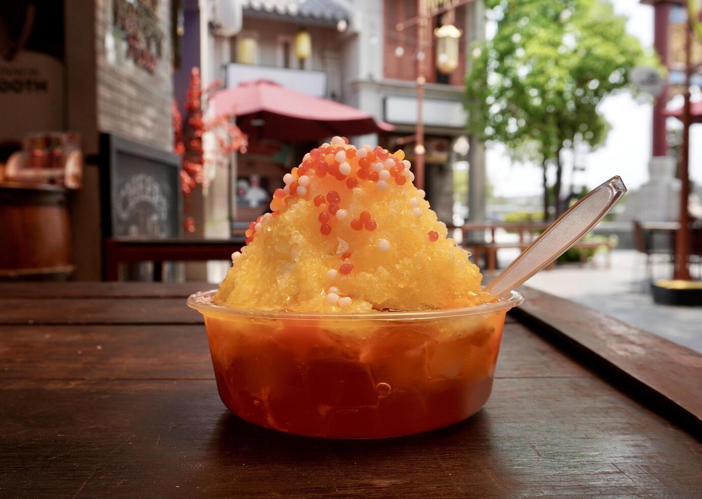 Sweet mango shaved ice dessert with popping jelly topping isolated on horizontal ratio outdoor food court wooden table background. photo