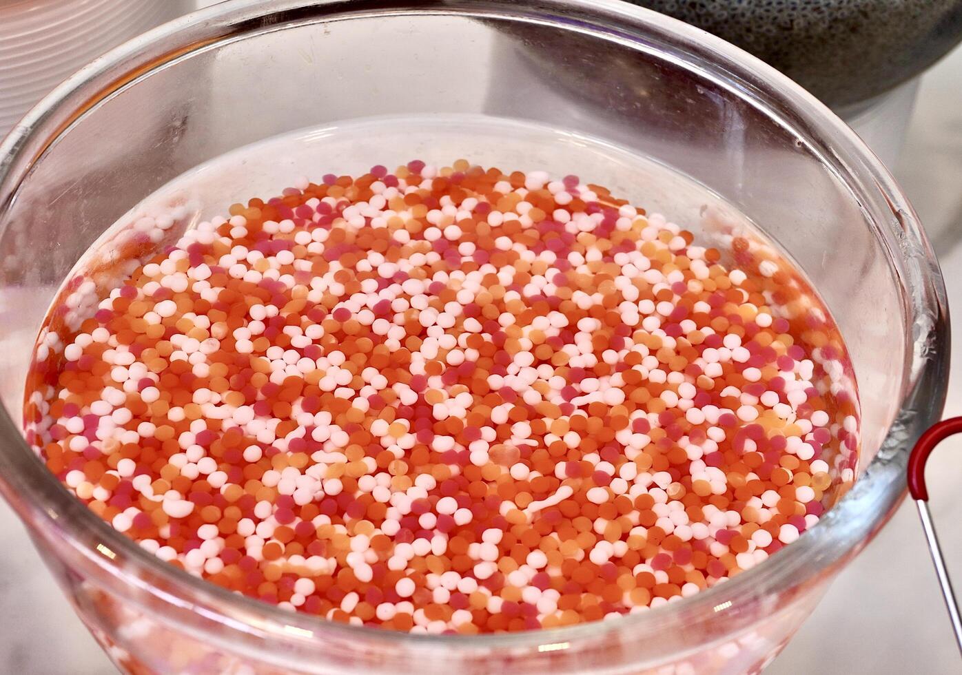 Sweet and delicious small round white, orange, and red jelly dessert toppings in glass bowl isolated on horizontal ratio white table background. photo