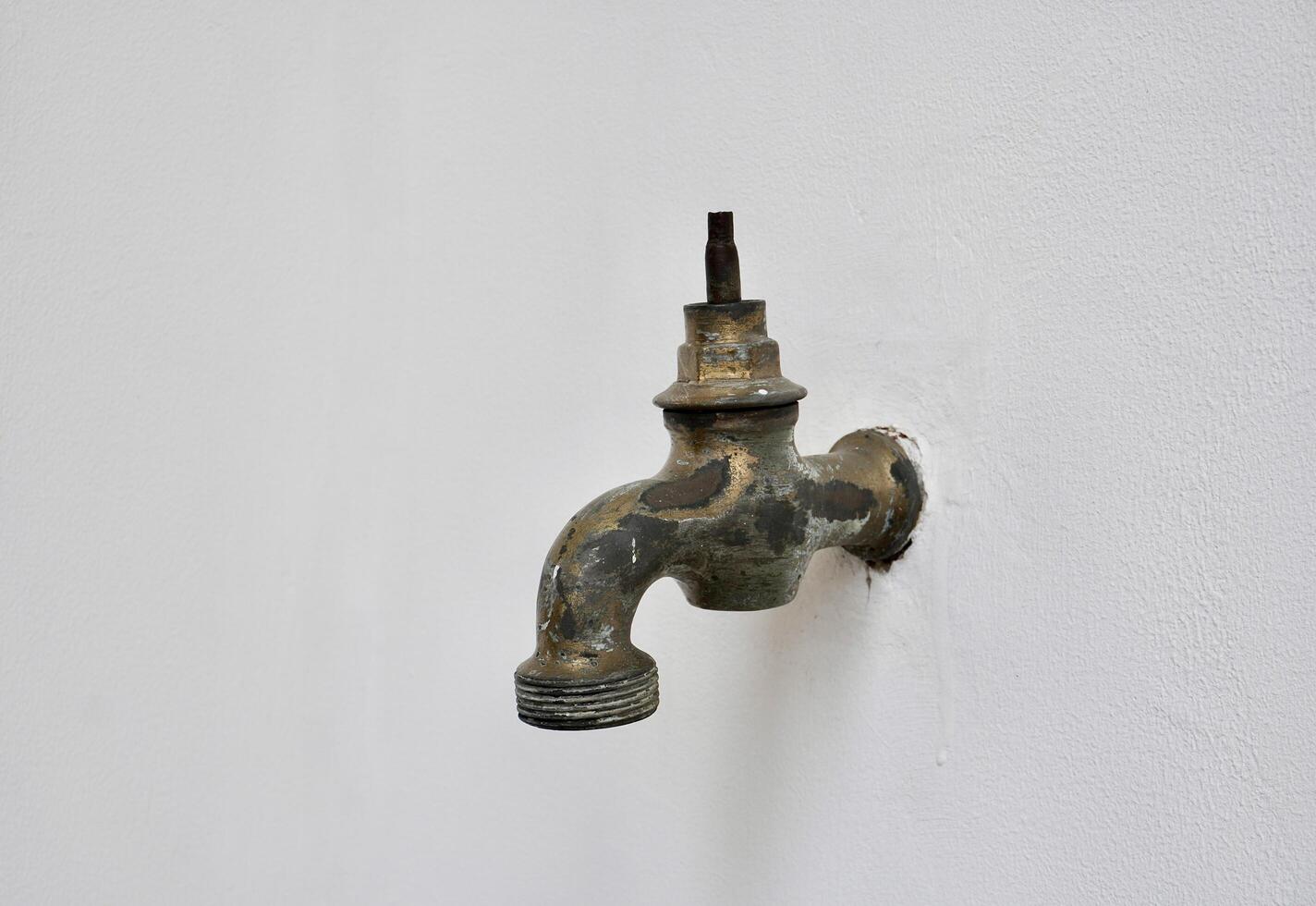 Old and aged rusty iron water faucet with missing valve handle part isolated on horizontal ratio white wall background. photo