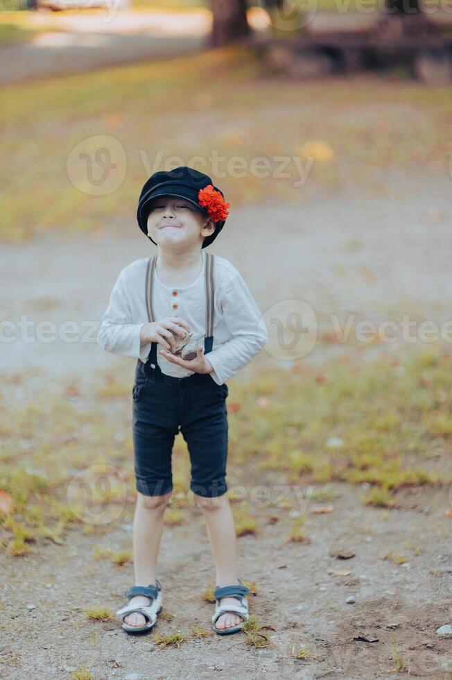 Funny little boy in retro hat with red flower holding pebbles photo