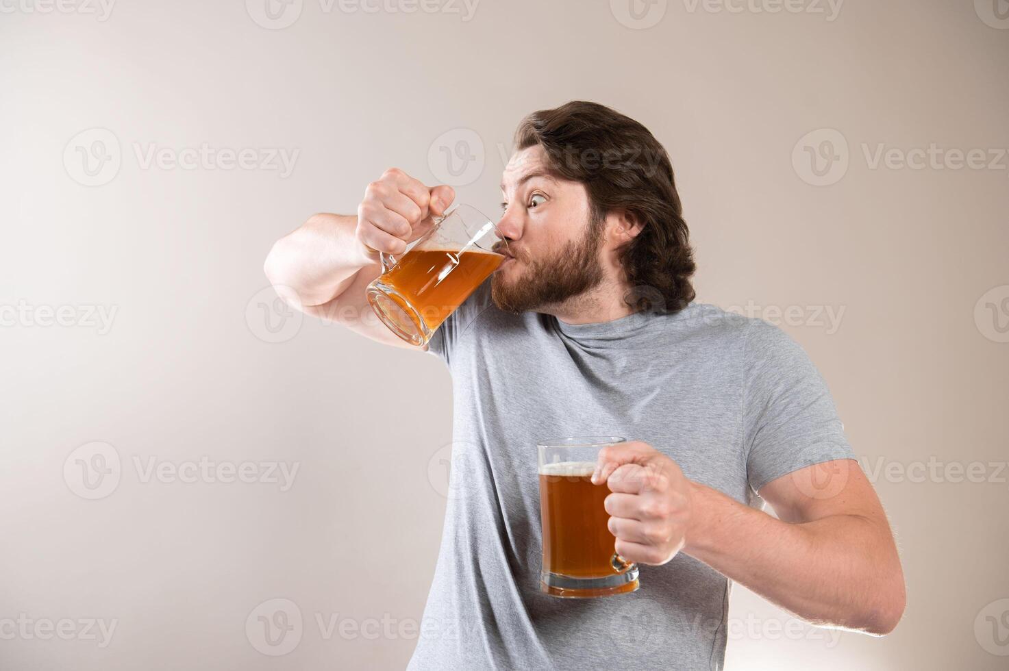 Young man drinking beer isolated on gray studio background, excited expression photo