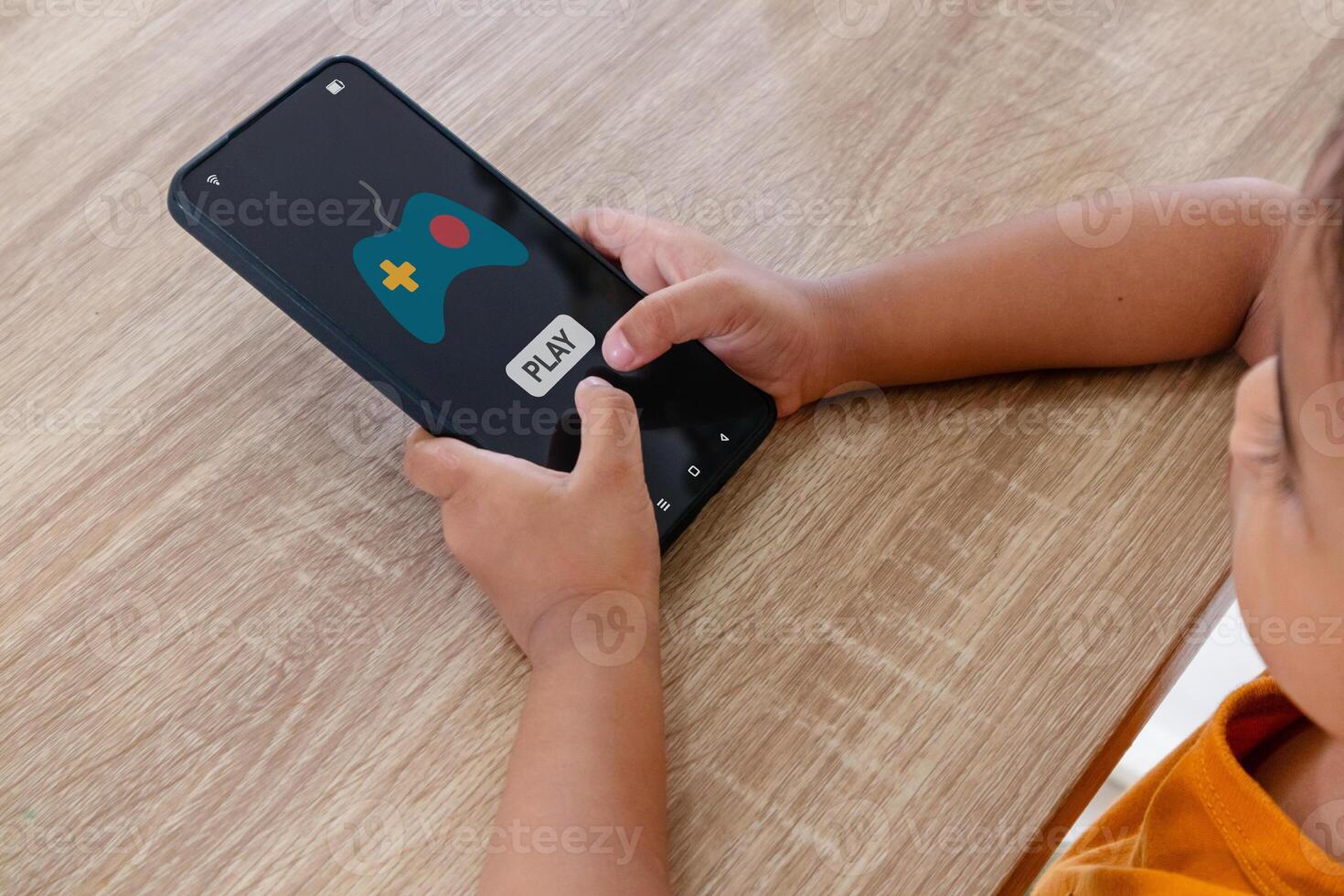 A little Asian girl sitting at table and playing games on her smartphone photo