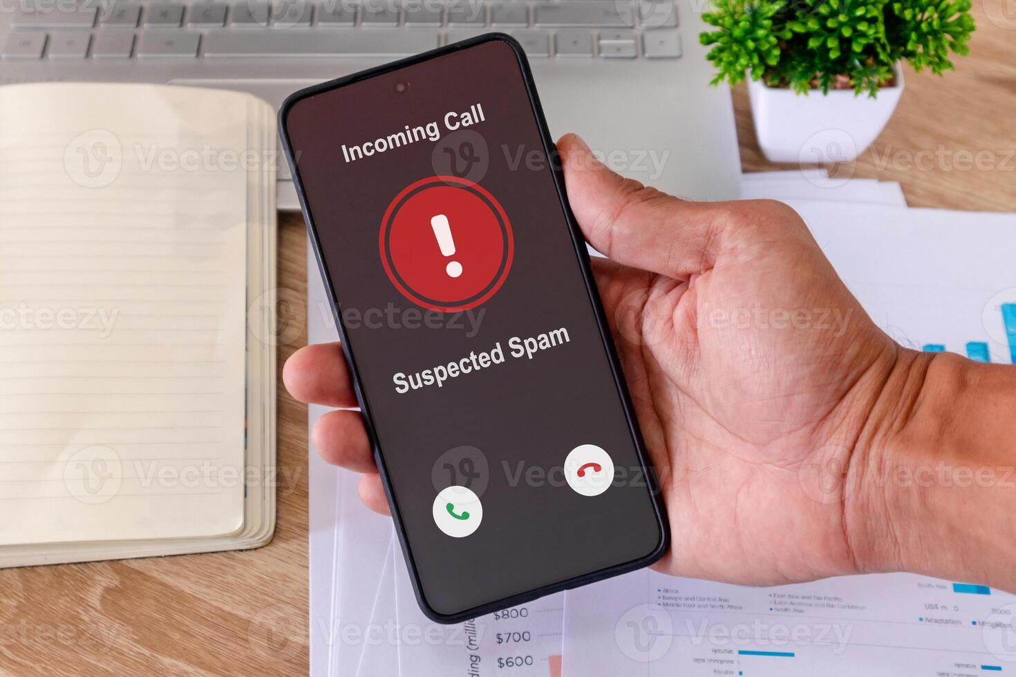 Hand holding a smartphone with incoming call from unknown caller on the screen at workplace. Spammer incoming call concept. photo