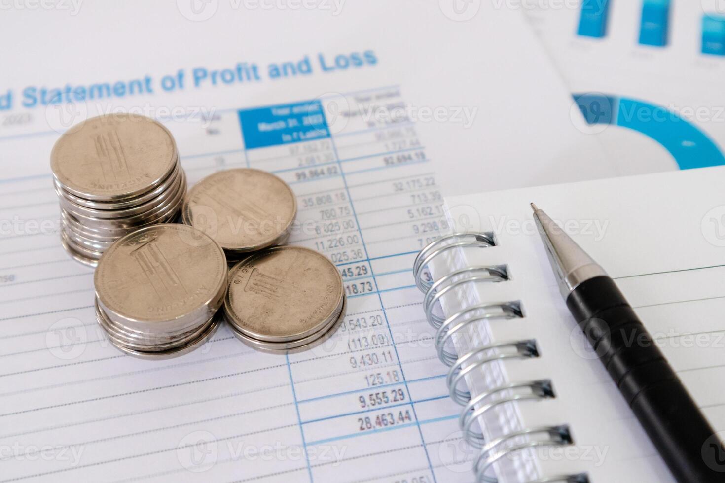 Close up view of stack of coins, notebook, and pen on top of financial data paperwork photo