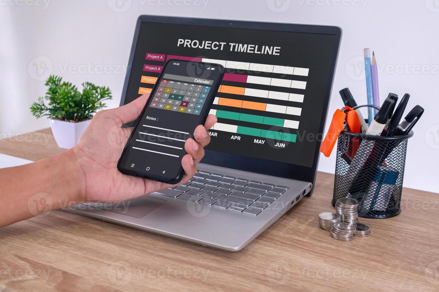 Male hand using a calendar app on smartphone to check the project timeline, milestones and planning progress on laptop photo