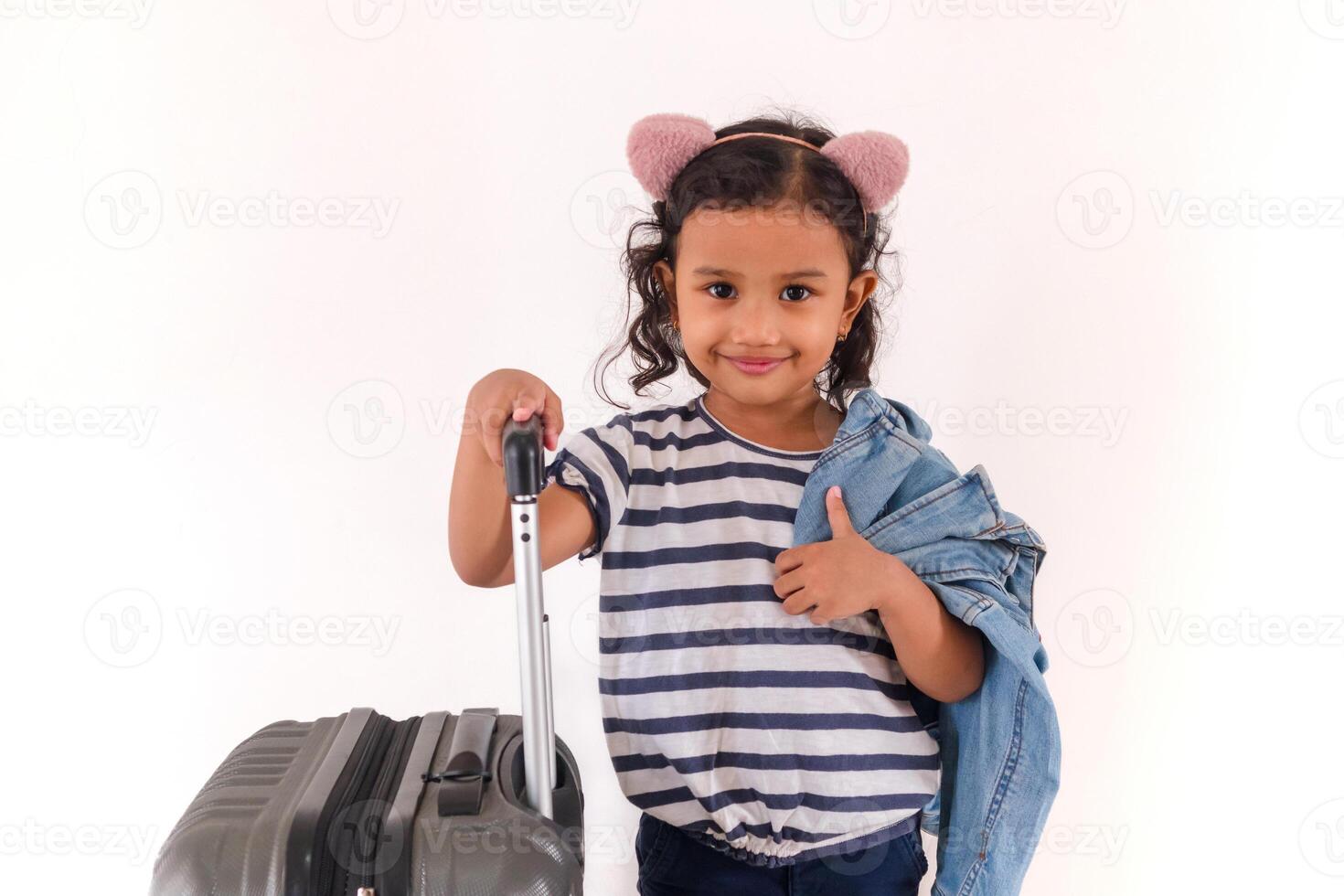 A little Asian girl smiling while holding a jacket on her shoulders and her suitcase photo