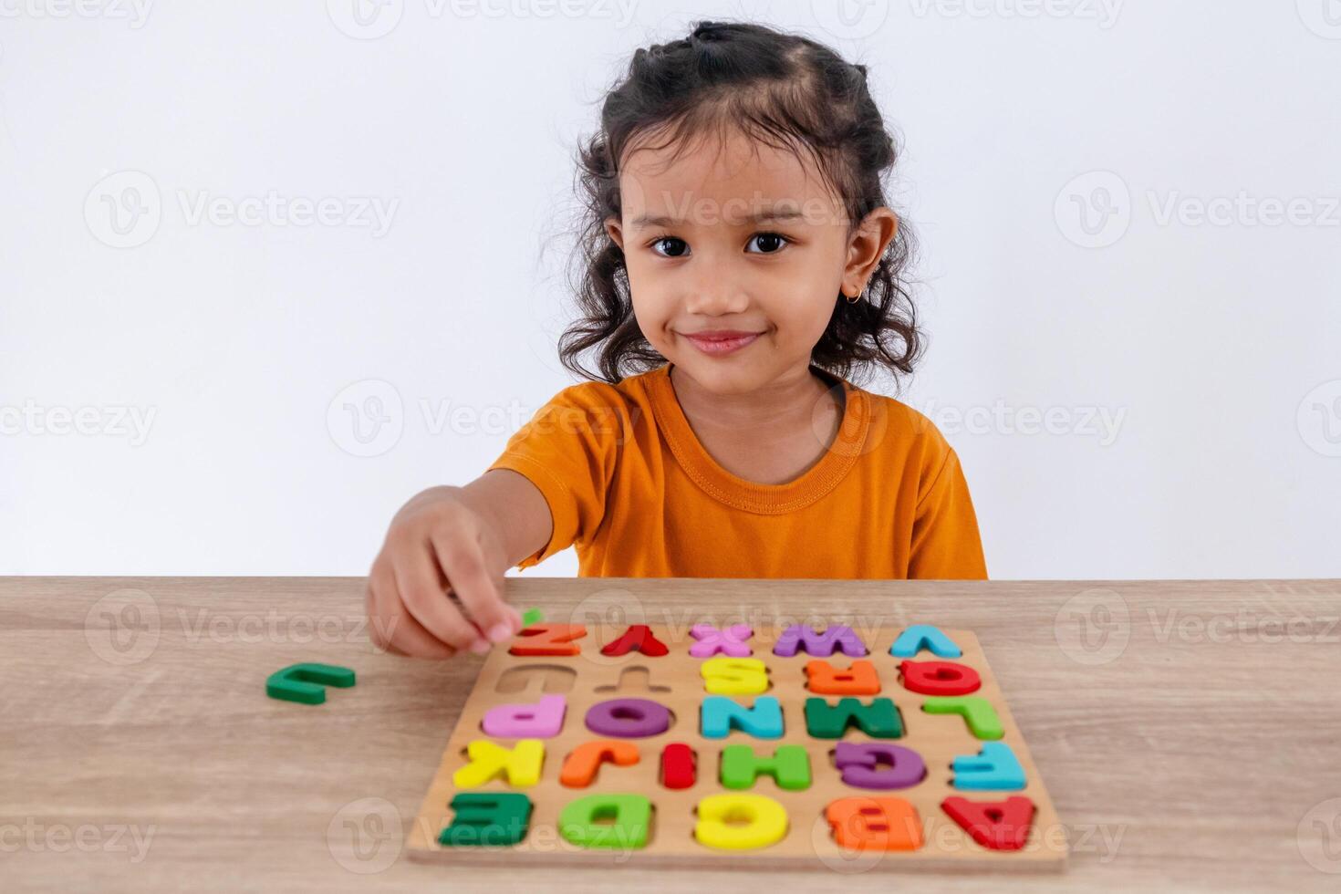 A little Asian girl arranges colorful wooden alphabet letters on a table photo