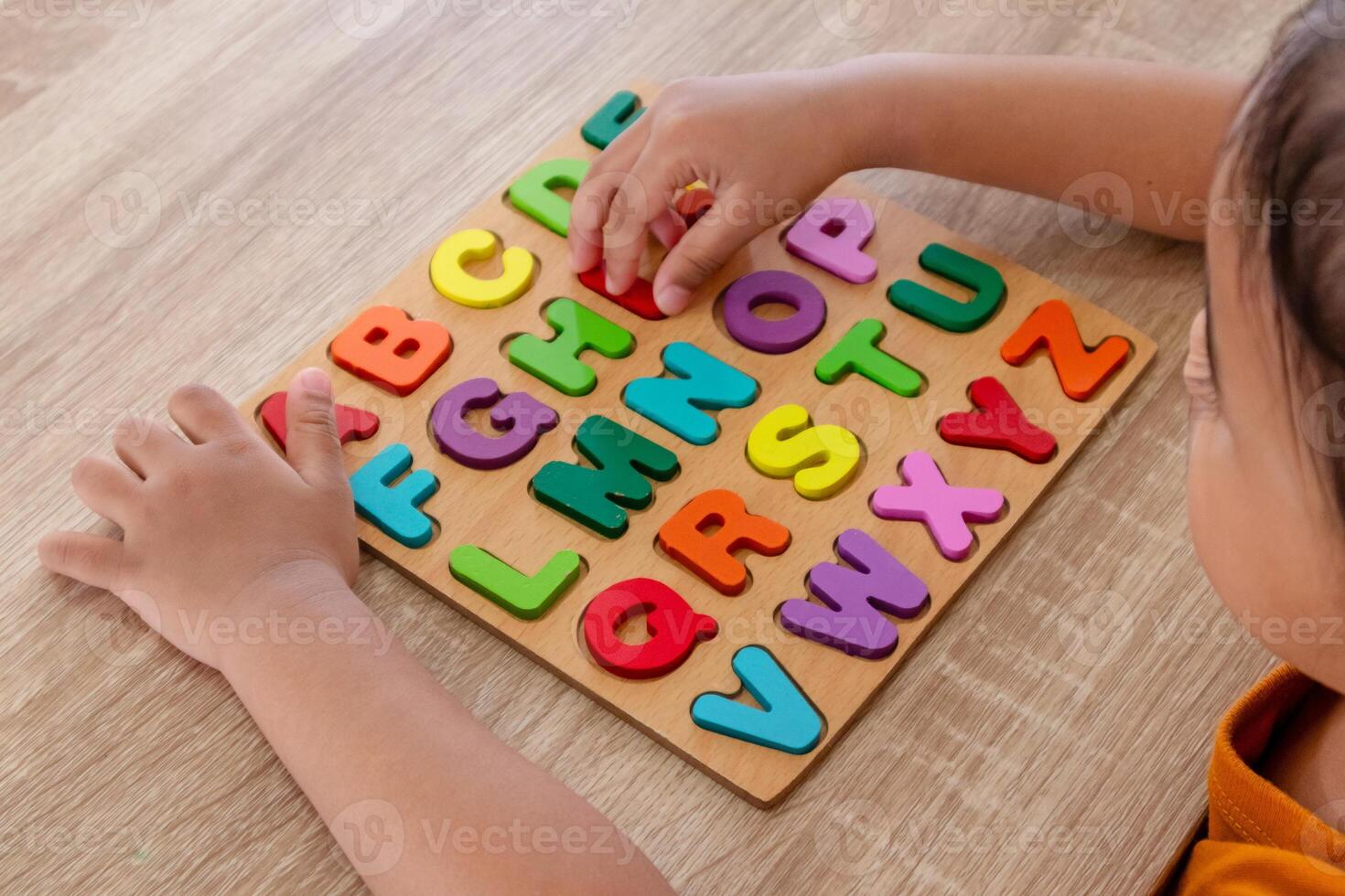 A little Asian girl assembles wooden alphabet letters puzzle on a table photo