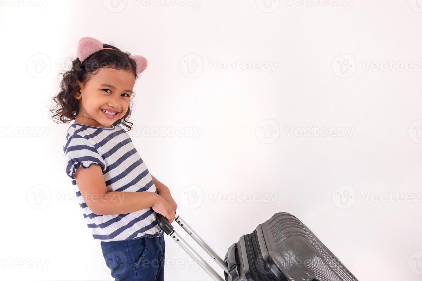 A happy little Asian girl posing with wear headband while pulling a suitcase photo