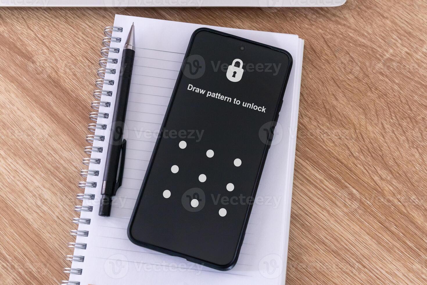 A locked smartphone on top of a notebook on a wooden table with drawing pattern to unlock screen photo