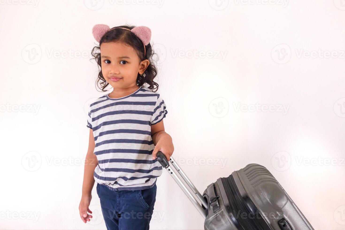 A cheerful little Asian girl posing with a suitcase. Travel or holiday concept. photo