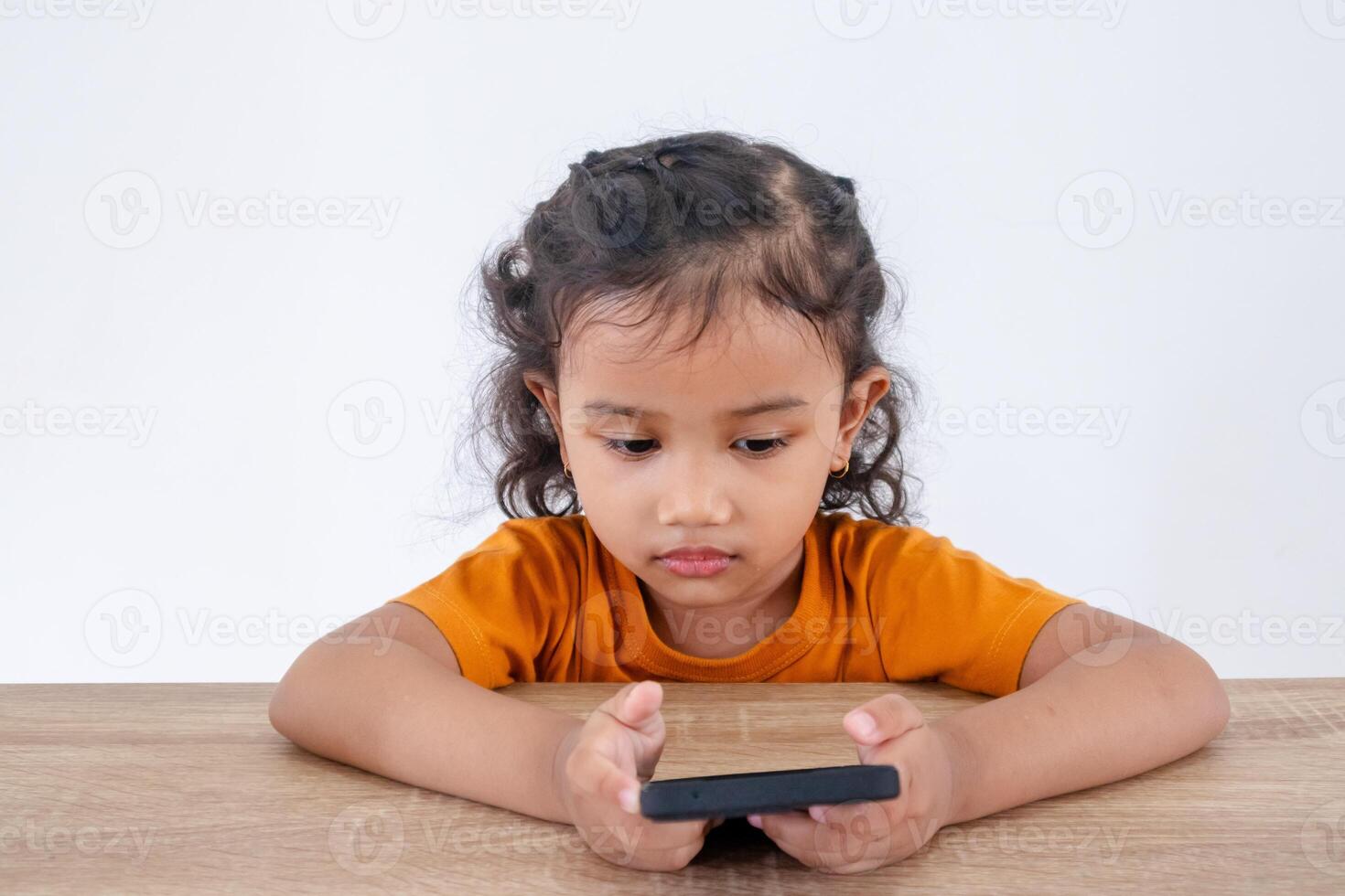 A little Asian girl sitting at table with a serious face and looking at her mobile phone photo