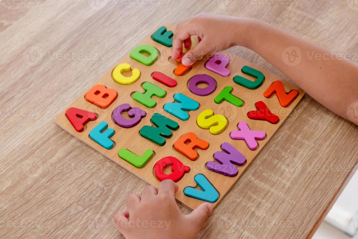 Hands of little girl assembles wooden alphabet letters puzzle on a table photo