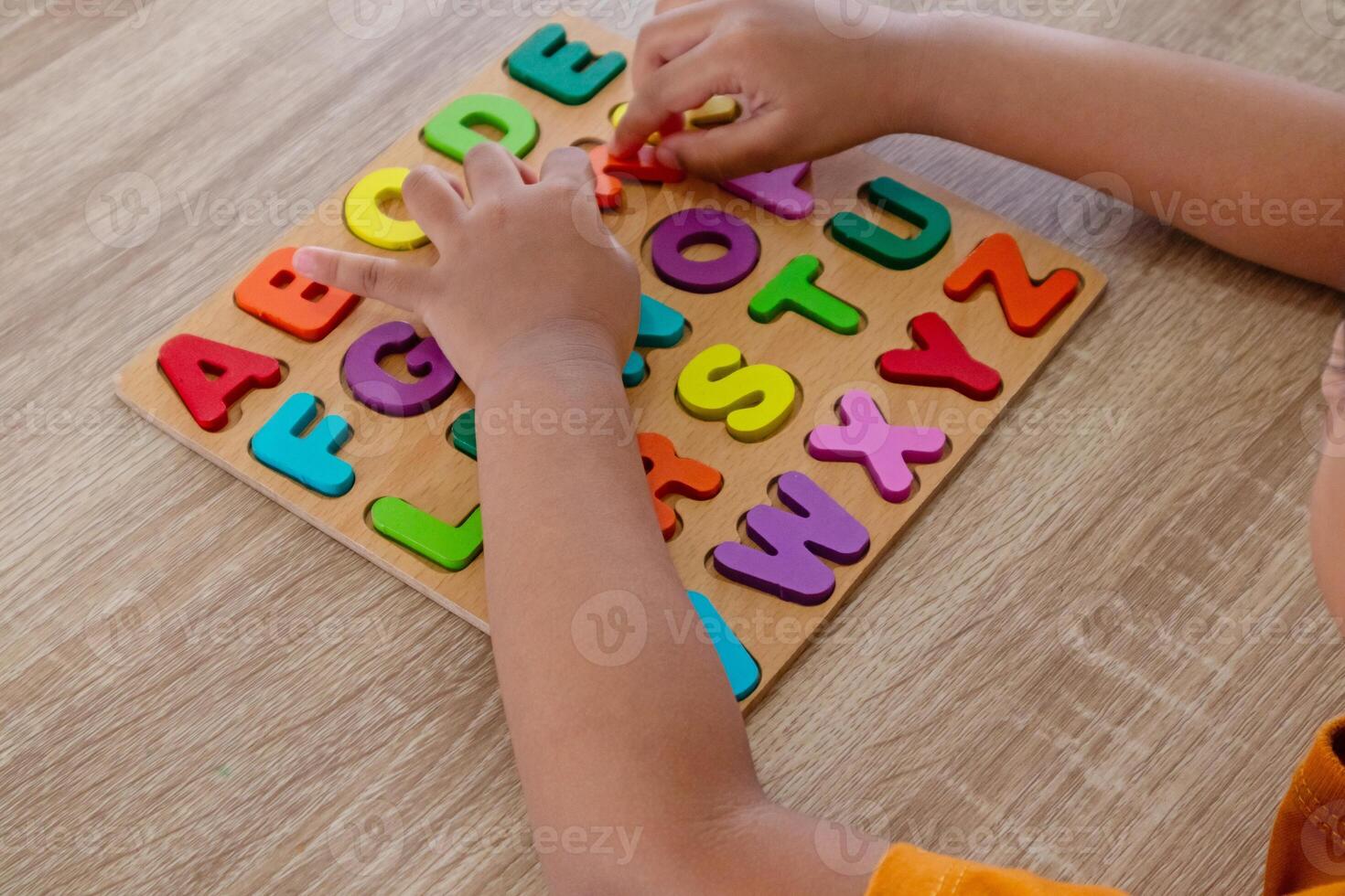 View of a little Asian girl plays with wooden alphabet letters puzzle on a table photo