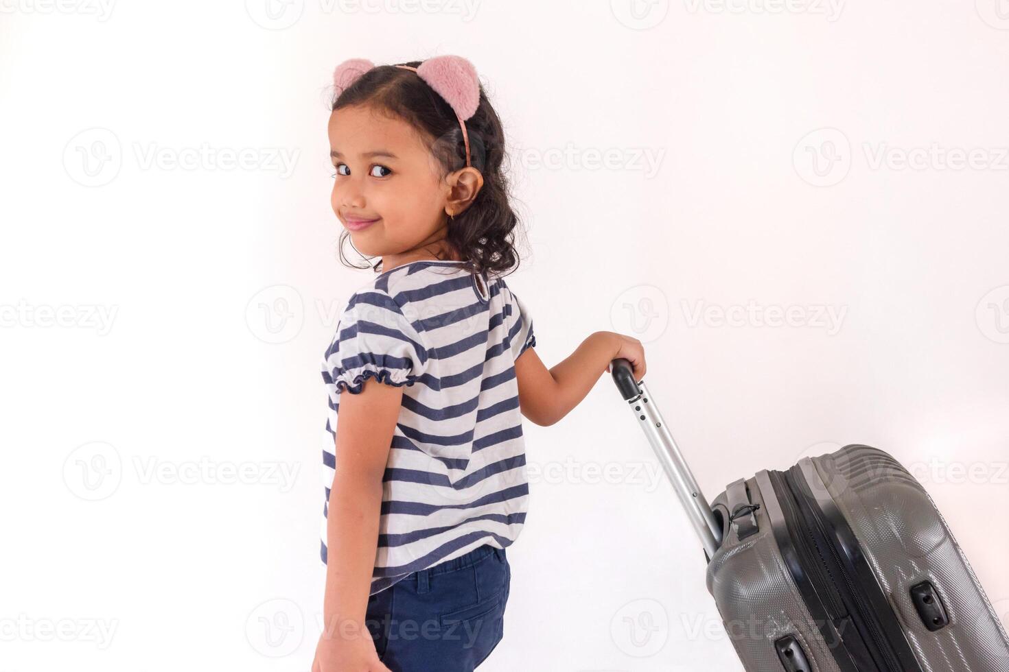 A cute little Asian girl wearing a headband and posing while pulling a suitcase photo