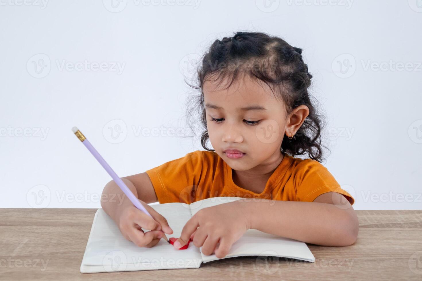 A little Asian girl sitting at table and learning to write in a notebook photo