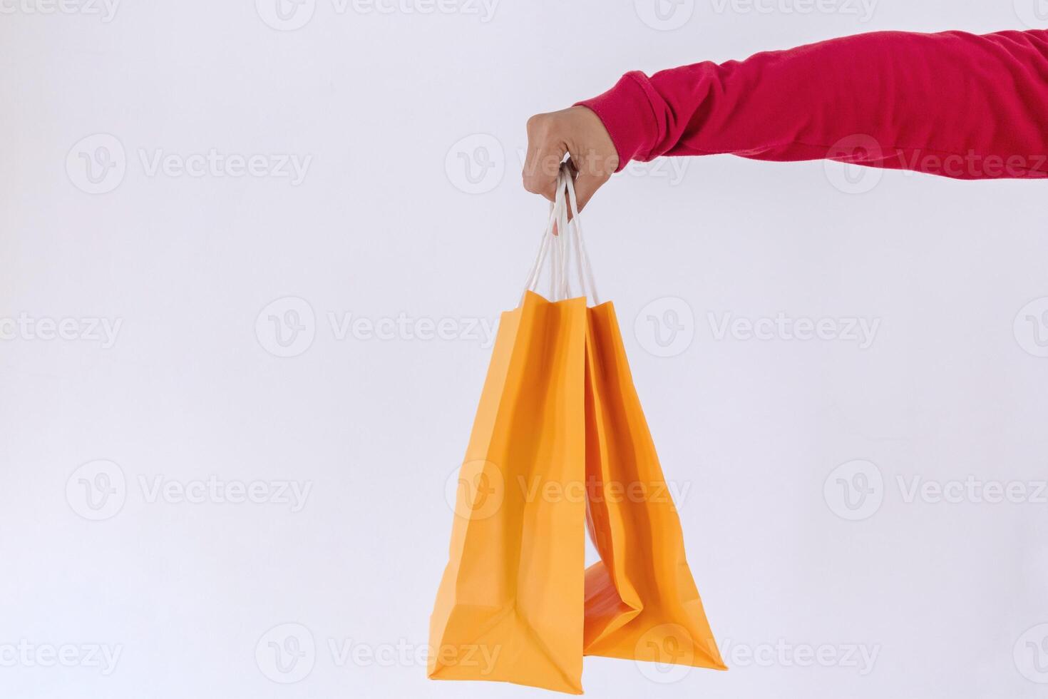 Close up view of a female hand with red long sleeve t-shirt holding two yellow paper shopping bags photo