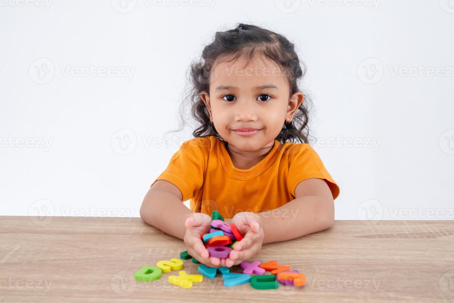 A happy little girl sitting at table with handful of wooden alphabet letters in palm photo