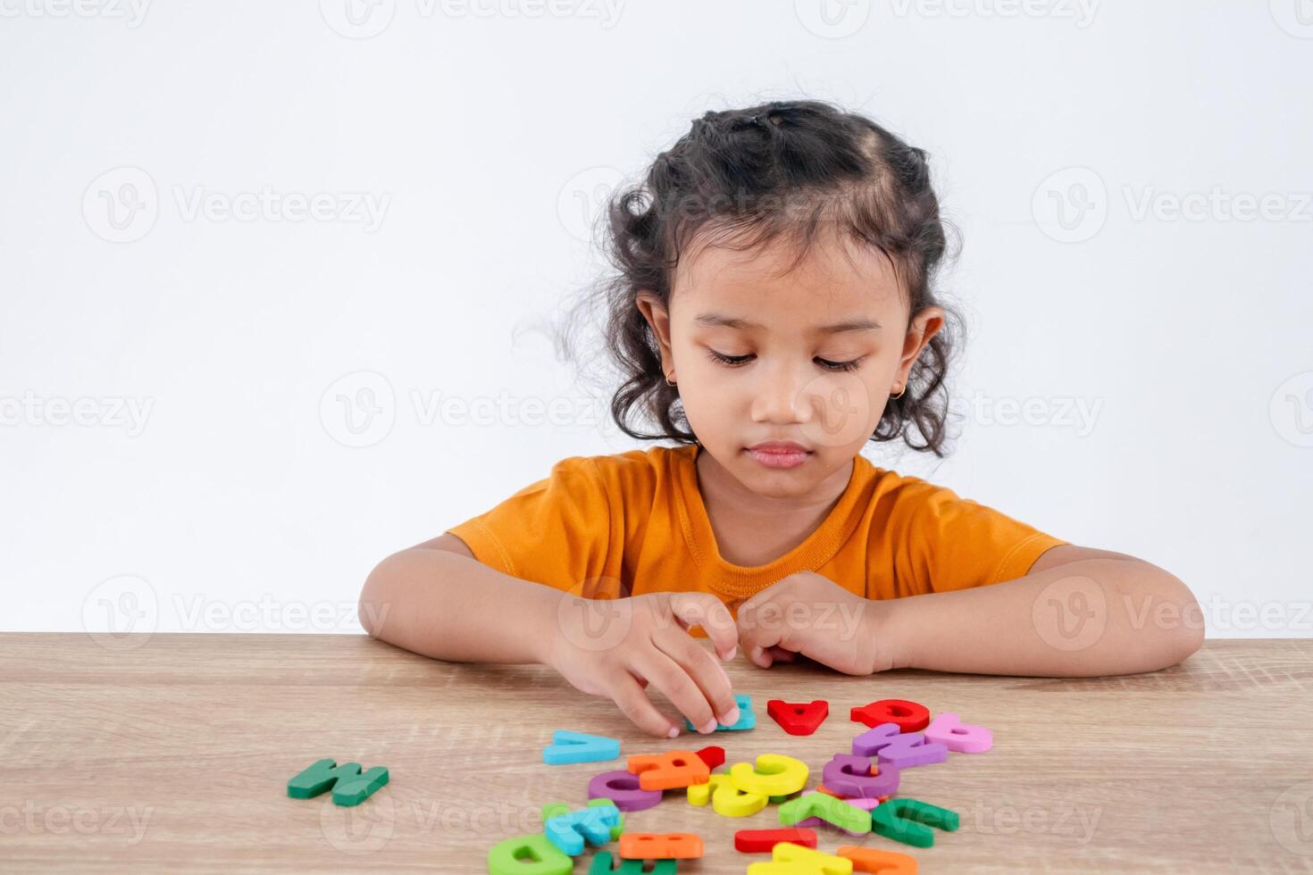 A cheerful little Asian girl enjoying playing with the wooden alphabet letters on the table photo