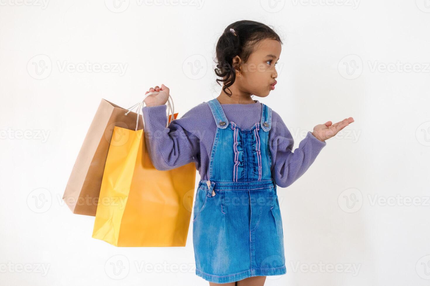 Excited little Asian girl looking and pointing at something to the side while holding a paper shopping bag photo