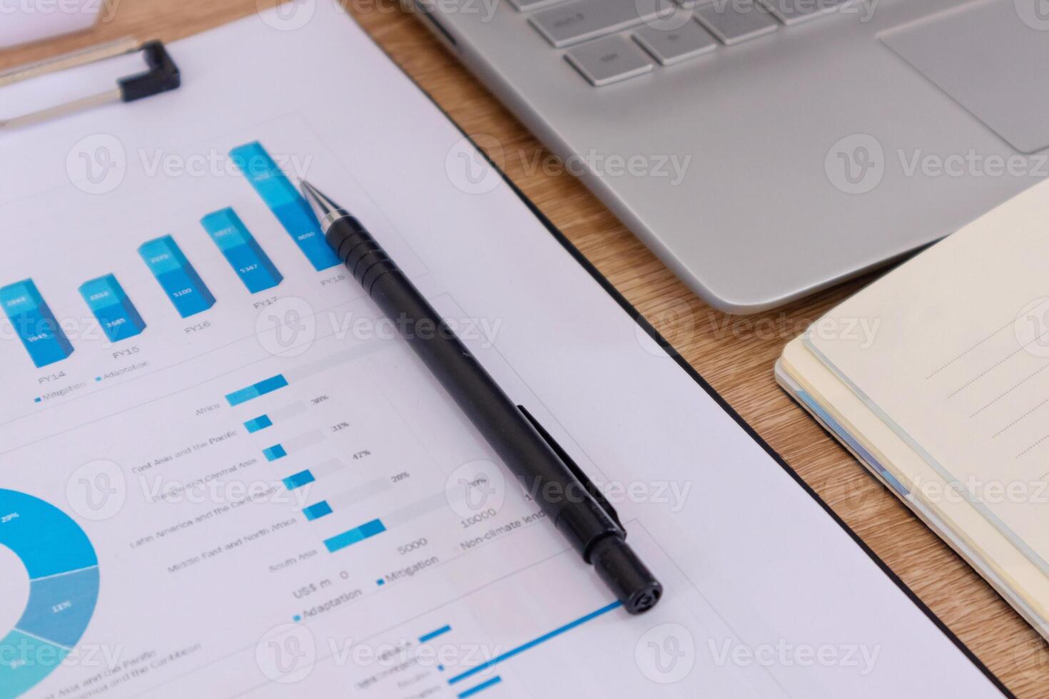 Close up view of workplace with notebook, pen, laptop, and paperwork or report photo