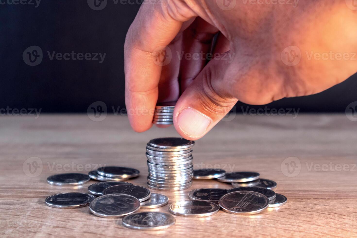 Man hand putting coins on stack on wooden table photo