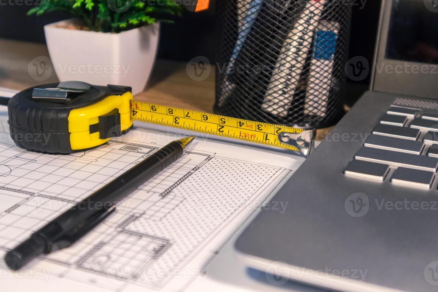 An architect's work desk with building layouts, stationery, pencil, and roll up metal tape measure photo