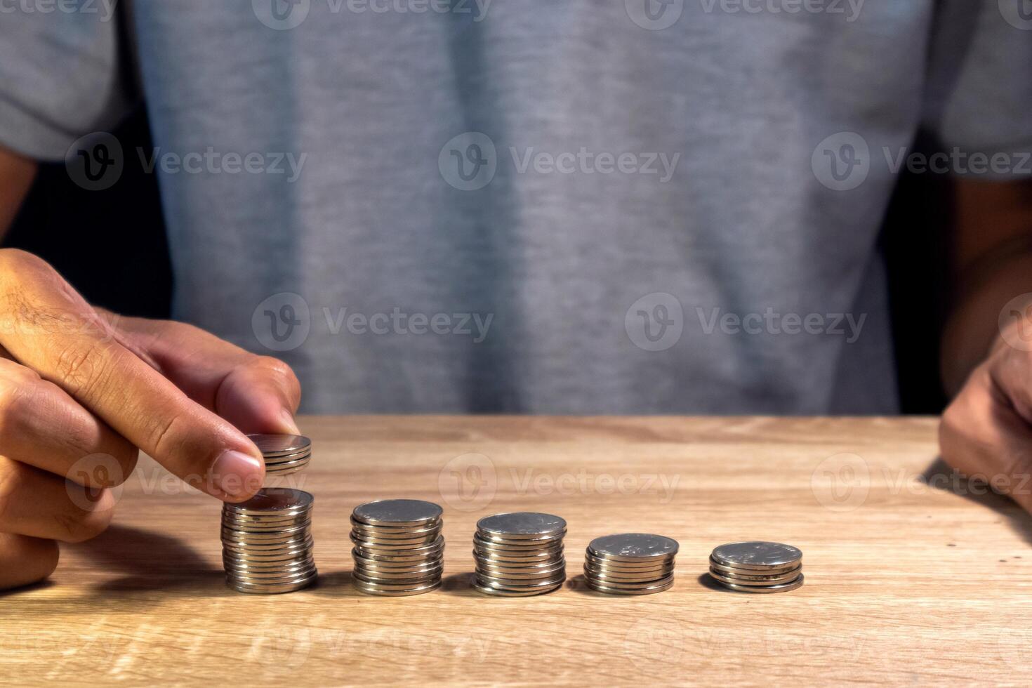 Man makes stacks of coins on wooden table to calculate cost or budget photo