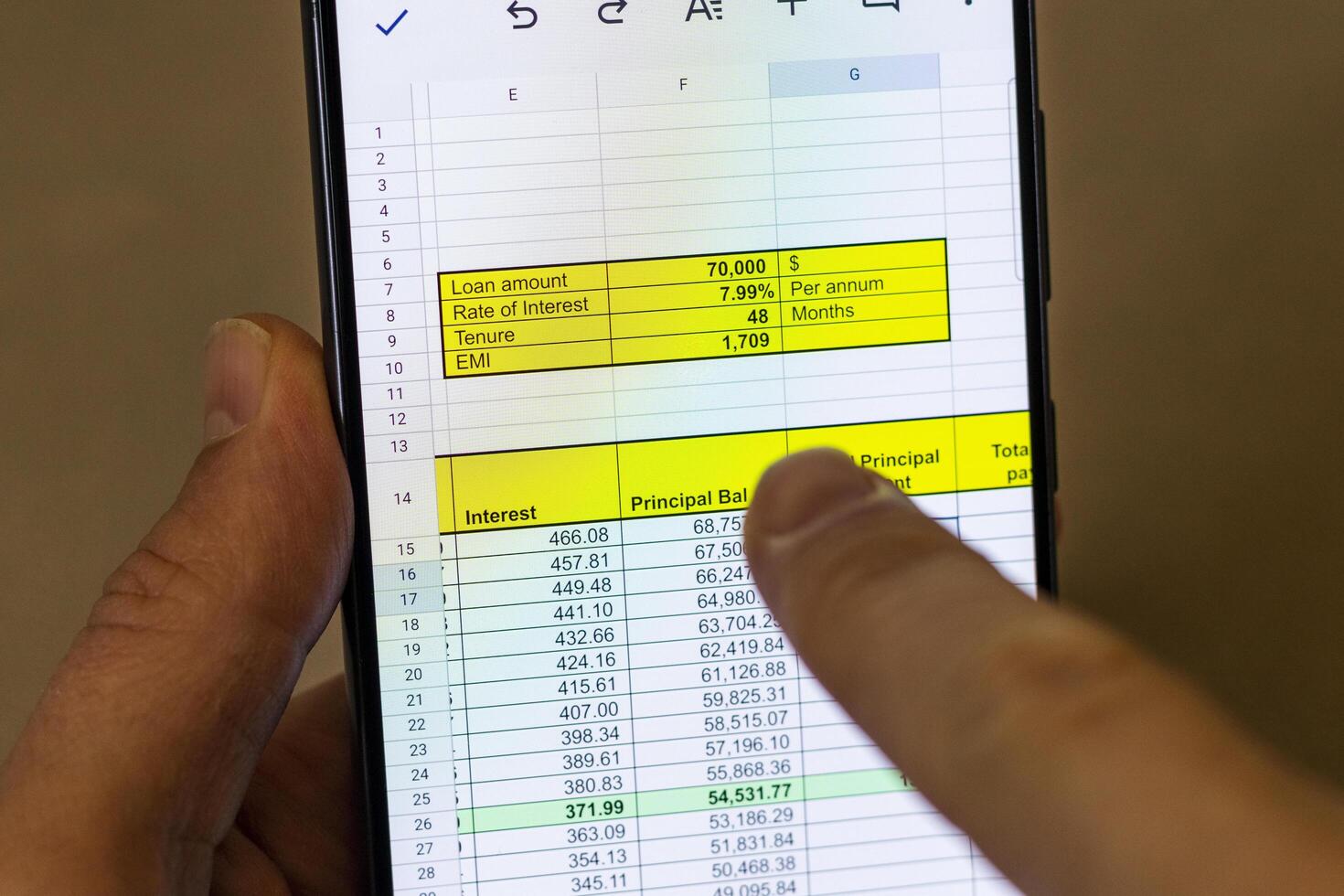 Man scrolling an excel sheet on the phone screen showing bank loan amortization table. Banking photo