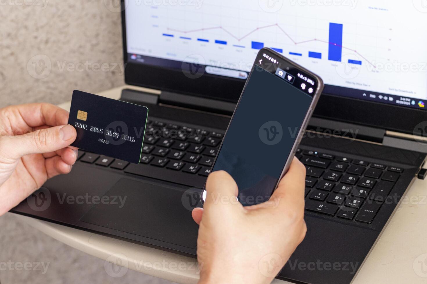 Shot of the man in the front of the laptop screen, holding credit card and the phone. Technology photo