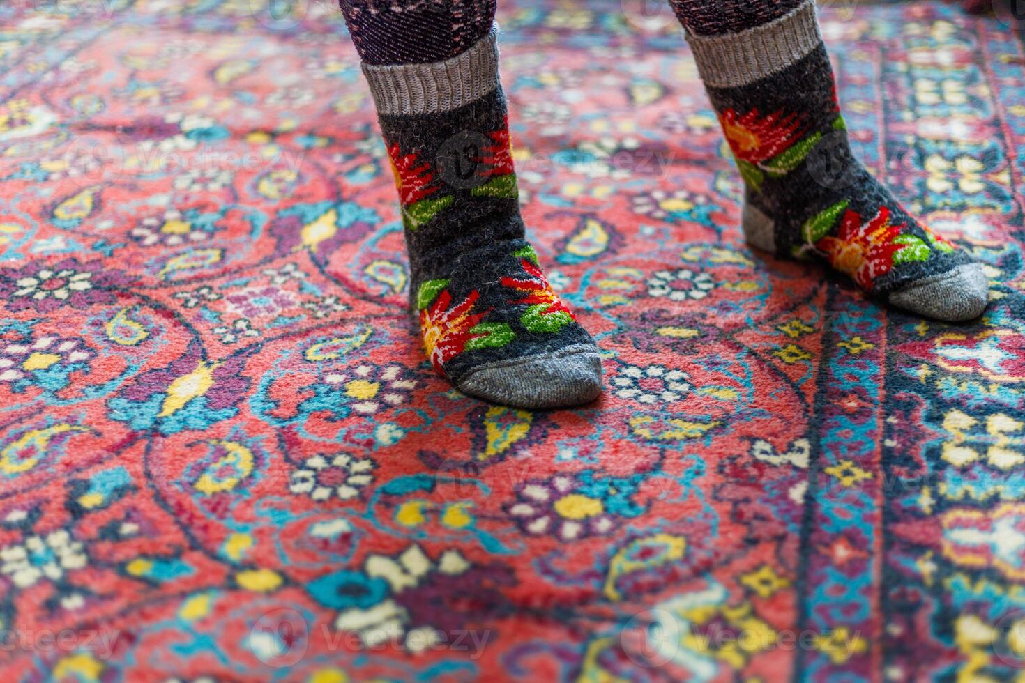 legs in warm woven wool socks standing on red ornate carpet floor at home photo