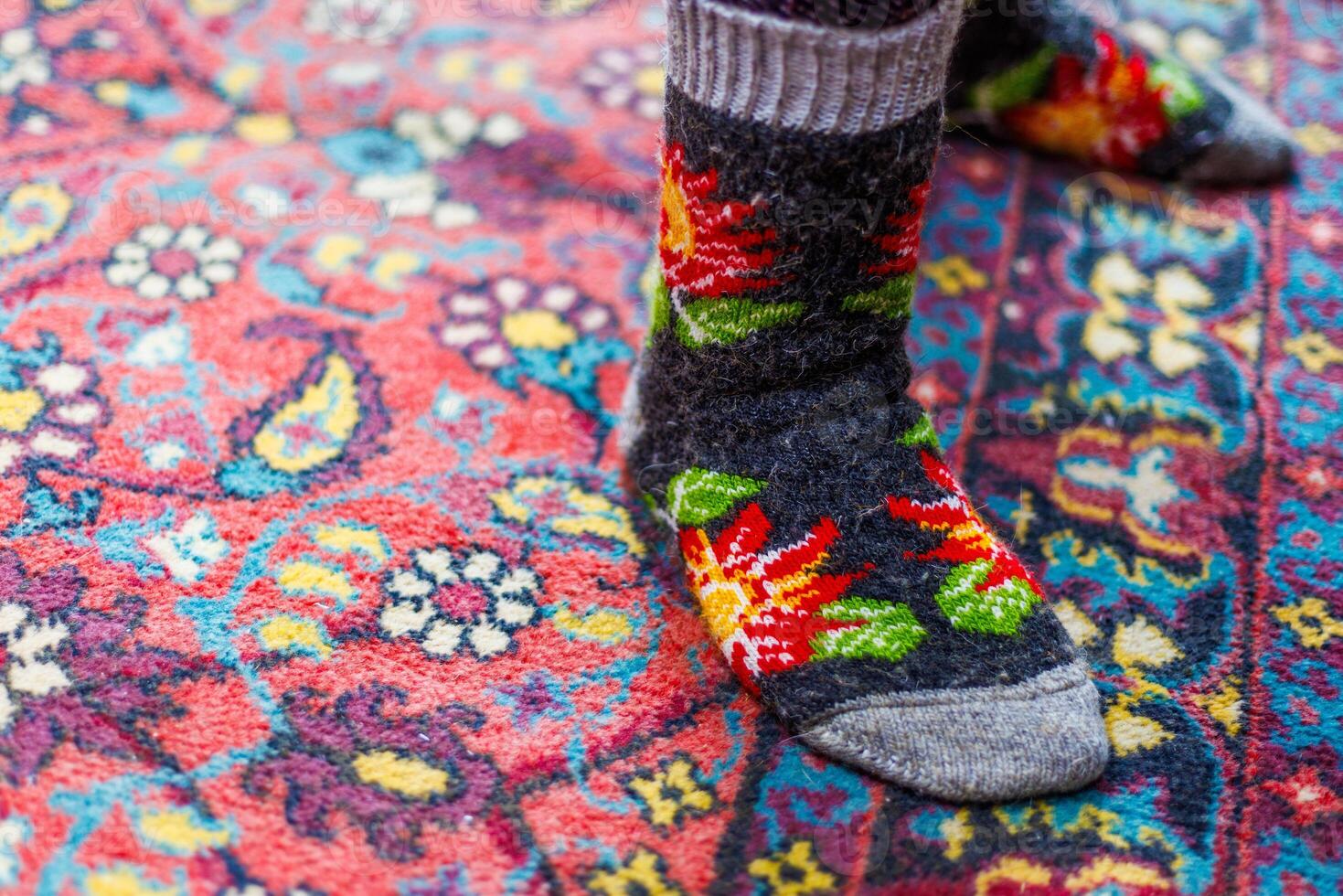 legs in warm woven wool socks standing on red ornate carpet floor at home photo