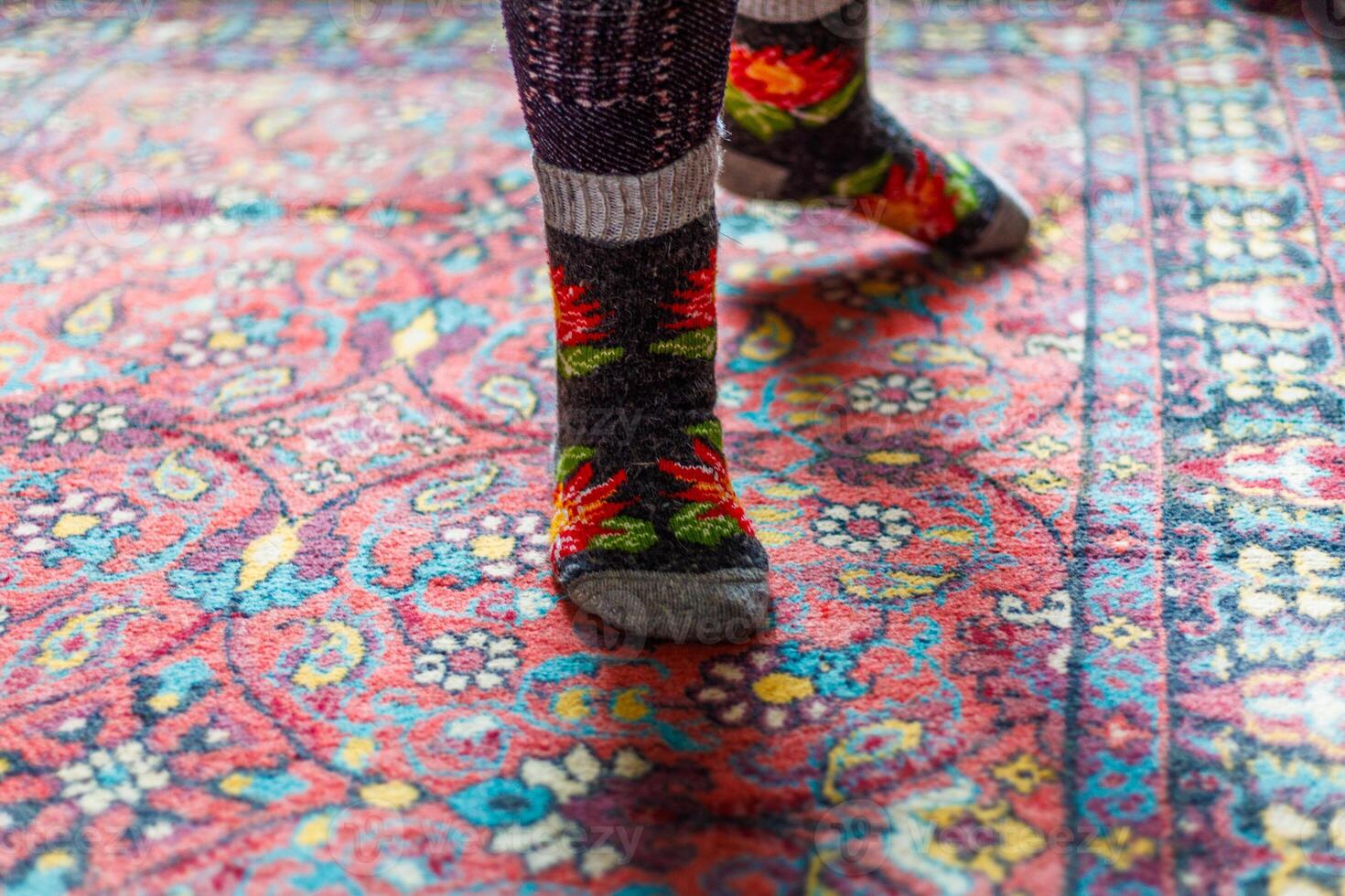 legs in warm woven wool socks standing on red ornate carpet floor at home photo