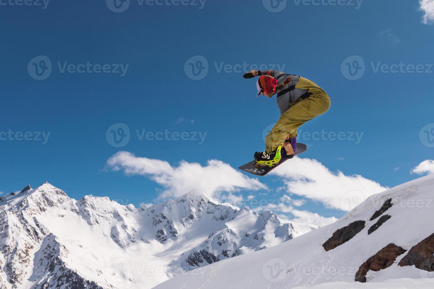 young woman snowboarder jumping from a springboard in the snowy mountains photo