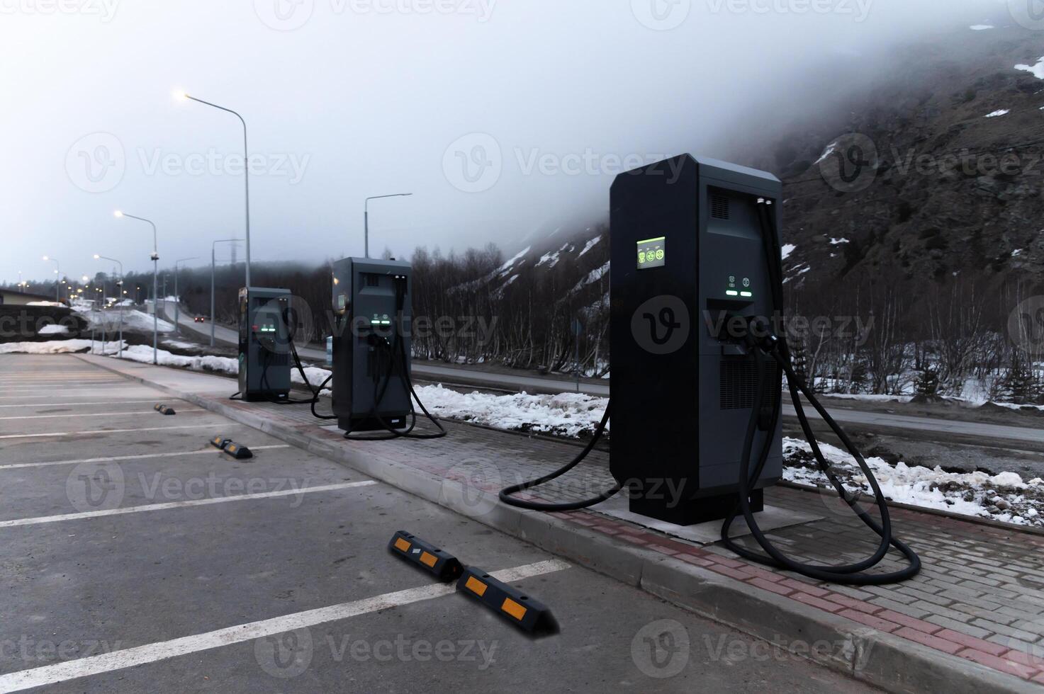 Electric car charging station, row of gas stations stands against the backdrop of mountains in fog in winter, cloudy weather photo