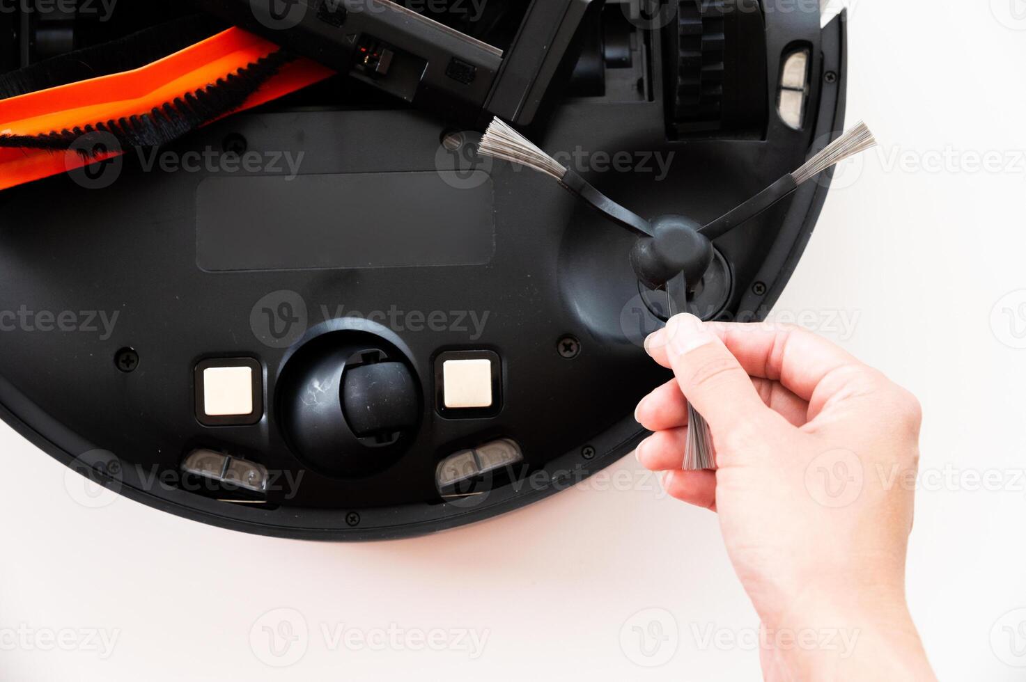 Maintenance of a smart robot vacuum cleaner. Women's hands maintain and clean a round robot vacuum cleaner. Organization of uninterrupted operation of a home cleaner photo