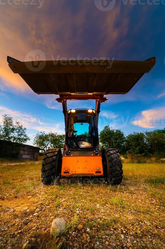 Mini bulldozer, small excavator against the backdrop of the sunset sky in the forest, wide angle photo