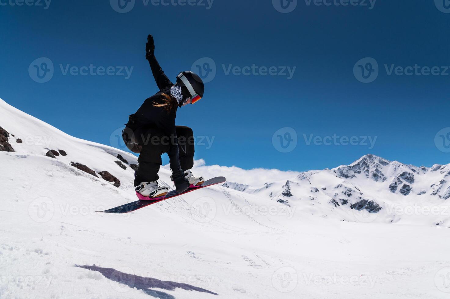 young woman snowboarder jumping from a springboard in the snowy mountains photo