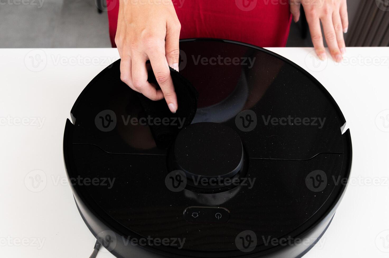 Robot vacuum cleaner with round black body on white background table, new home assistant, woman hand reaches out to turn it on and check, close-up photo